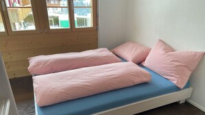 Een bed met een blauwe matras en roze kussens in een kamer met houten vloeren en een raam.