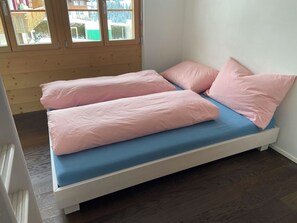 A bed with a blue mattress and pink pillows in a room with wooden flooring and a window. - Mühleport Appartement/Fewo, Bad, WC, 1 Schlafraum 2.5-Zimmerwohnung by Interhome (Adelboden)