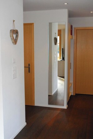 Un couloir avec des portes en bois, un miroir et un interrupteur sur le mur.