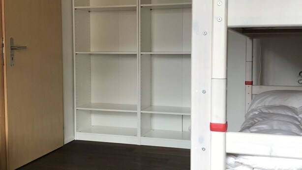 Een kamer met een stapelbed, een garderobe met meerdere planken en een houten deur.
