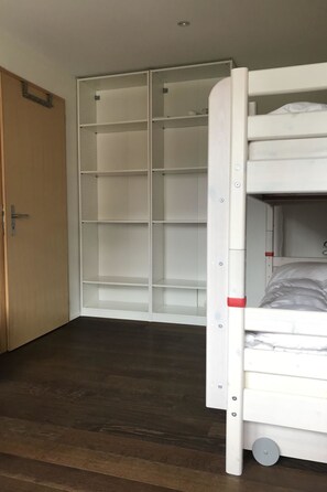 Een kamer met een stapelbed, een garderobe met meerdere planken en een houten deur.