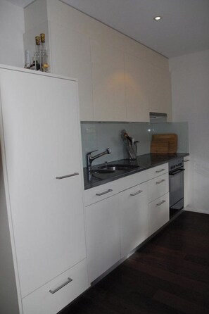 A modern kitchen with white cabinetry, a black countertop, and a built-in oven. - Mühleport Appartement/Fewo, Bad, WC, 1 Schlafraum 2.5-Zimmerwohnung by Interhome (Adelboden)