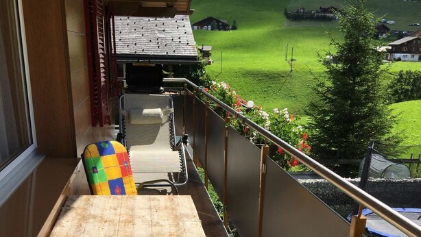 Un balcón con una mesa de madera y dos sillas, una con un cojín colorido.