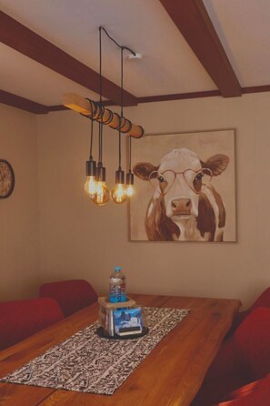 A dining area with a wooden table, red cushioned chairs, a water bottle, and a framed picture of a cow on the wall. - Aloa Appartement/Fewo, Bad, WC, 2 Schlafräume 3.5-Zimmerwohnung by Interhome (Adelboden)