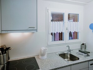 Una cocina moderna con estufa integrada, un lavamanos y un ventanal con cortinas blancas.