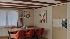 Una sala moderna con una mesa de comedor de madera, sillas rojas, una mesa redonda de centro y una cocina con alacenas y un refrigerador.