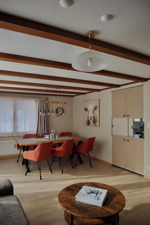 Ein modernes Wohnzimmer mit einem Holzespeisetisch, roten Stühlen, einem runden Couchtisch und einer Küchenzeile mit Schränken und einem Kühlschrank.