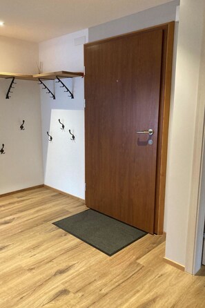 Una habitación con puerta de madera, felpudo negro y ganchos en la pared.