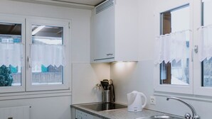 Una cocina moderna con armarios blancos, un lavamanos de acero inoxidable y un hervidor.