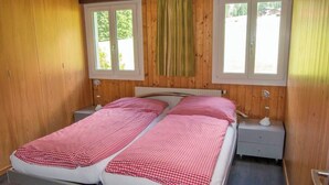 A double bed with checkered bedding in a room with wooden walls and two windows. - Chalet Bondertal Appartement/Fewo, Dusche, WC, 2 Schlafräume 3.5-Zimmerwohnung by Interhome (Adelboden)