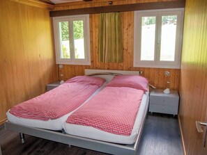 Ein Doppelbett mit karierter Bettwäsche in einem Zimmer mit Holzwänden und zwei Fenstern.