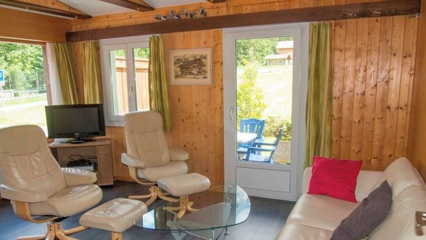 A furnished room with a sofa, two chairs, a glass coffee table, a television, and a window with curtains. - Chalet Bondertal Appartement/Fewo, Dusche, WC, 2 Schlafräume 3.5-Zimmerwohnung by Interhome (Adelboden)