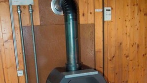 A wood-burning stove with a glass door, set against a wooden wall with a vent pipe above it. - Chalet Bondertal Appartement/Fewo, Dusche, WC, 2 Schlafräume 3.5-Zimmerwohnung by Interhome (Adelboden)