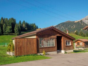Eine Holzhütte mit geneigtem Dach, großen Fenstern und einer kleinen Veranda.