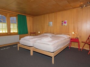 A room with a wooden bunk bed, a red chair, a small table with a lamp, and a window with green curtains. - Im Zentrum OG Appartement/Fewo, Dusche und Bad, WC, 2 Schlafräume by Interhome (Adelboden)