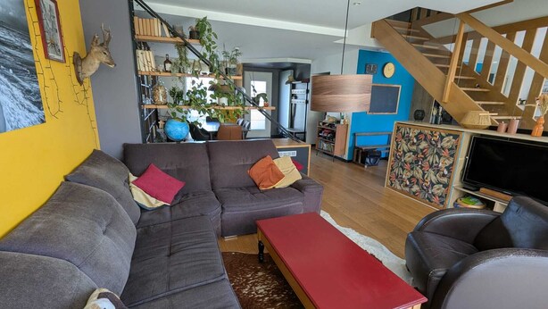En moderne stue med en hjørnesofa, et rødt sofabord og en trappe, der fører til en etage ovenpå.