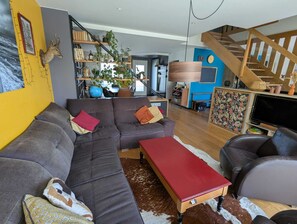 A modern living room with a sectional sofa, a red coffee table, and a staircase leading to an upper level. - Townhouse near the train station (15-minute walk) and Sillon Beach (25-minute walk). Ideal Route du Rhum (Saint-Malo)