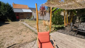 En træterrasse med en gyngestol, en træbygning med påskriften 'LA SARDINE', og en have med forskellige planter.