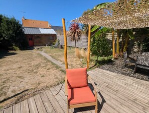 Eine Holzterrasse mit einer Schaukel, ein Holzgebäude mit der Aufschrift 'LA SARDINE' und ein Garten mit verschiedenen Pflanzen.