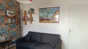 En stue med sofa, bogreol, plakat og dør.
