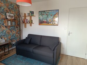 Ein Wohnzimmer mit einer Couch, einem Bücherregal, einem Poster und einer Tür.