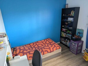 Ein kleines Zimmer mit einem Einzelbett, einem Schreibtisch und einem Bücherregal.