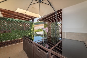 A covered outdoor seating area with a glass table, wicker furniture, and a view of the surrounding greenery. - Cavallo Residence (Torre Santa Sabina)