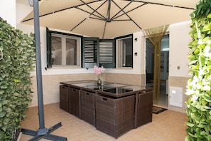 A corner kitchen area with a large umbrella, wicker furniture, and a vase with flowers. - Cavallo Residence (Torre Santa Sabina)