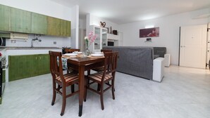 Eine moderne Küche mit grünen Schränken, einem Esstisch für vier Personen und einem grauen Sofa im Wohnbereich.