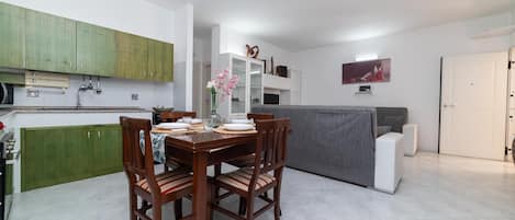 Una cocina moderna con armarios verdes, una mesa de comedor para cuatro personas y un sofá gris en la sala de estar.