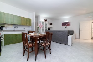 A modern kitchen with green cabinets, a dining table set for four, and a grey sofa in the living area. - Cavallo Residence (Torre Santa Sabina)