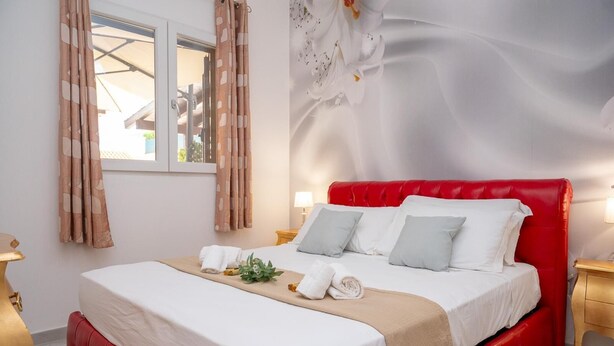 Ein Hotelzimmer mit einem rot gepolsterten Bett, weißer Bettwäsche, einem Fenster mit Vorhängen und einer Wand mit floralem Wandbild.