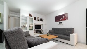 Ein modernes Wohnzimmer mit grauem Sofa, einem weißen Sessel, einem Holztisch und einem Flachbildfernseher.