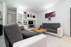 A modern living room with a grey sofa, a white armchair, a wooden coffee table, and a flat-screen TV. - Cavallo Residence (Torre Santa Sabina)