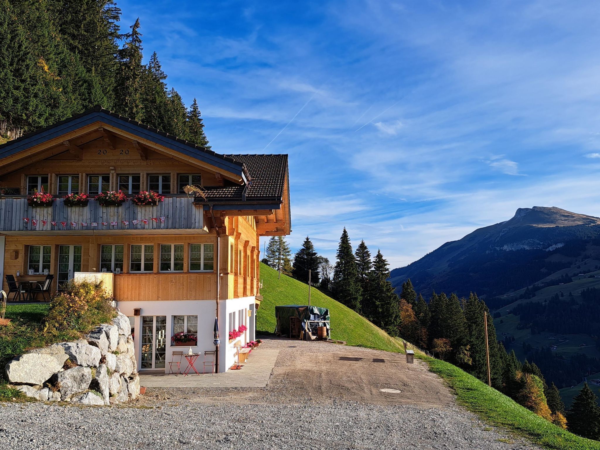 Un chalet de madera con balcón, camino de grava y montañas al fondo.