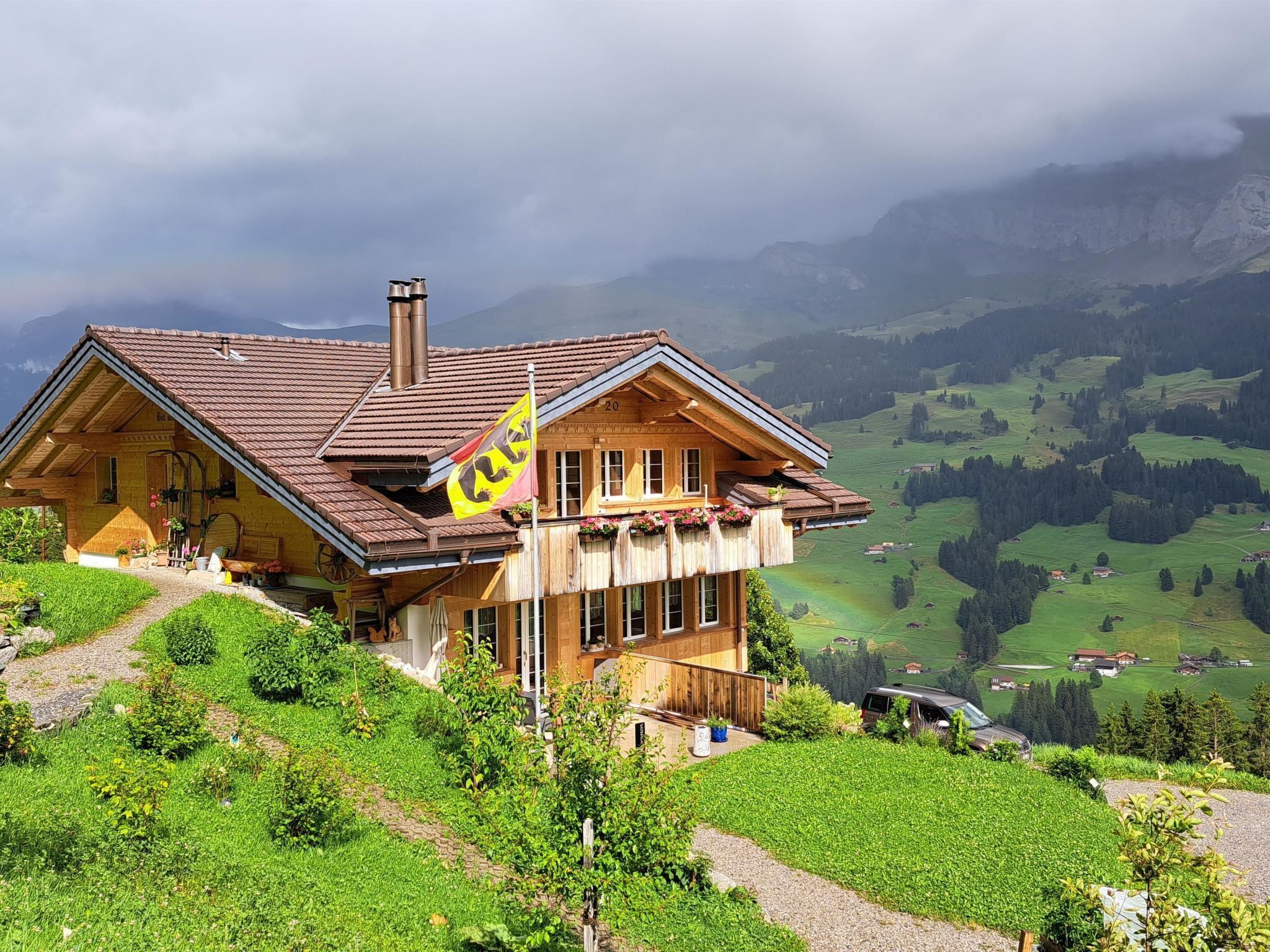 Een houten chalet met schuin dak, gelegen op een helling met uitzicht over een vallei en bergen.