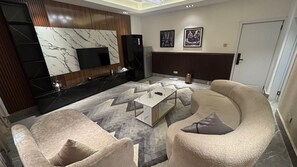 Ein modernes Wohnzimmer mit einer Wand im Marmor-Look, einem Flachbildfernseher, einem Sofa, einem Couchtisch und einer Tür.