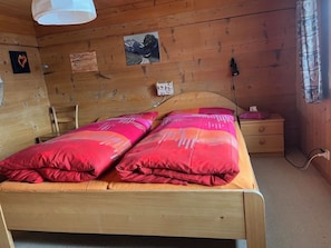 Ein Schlafzimmer einer Holzhütte mit einem Bett, einem Nachttisch und einer Wandleuchte.