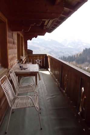 Ein Holzbalkon mit Tisch und Stühlen, der auf eine gebirgige Landschaft blickt.