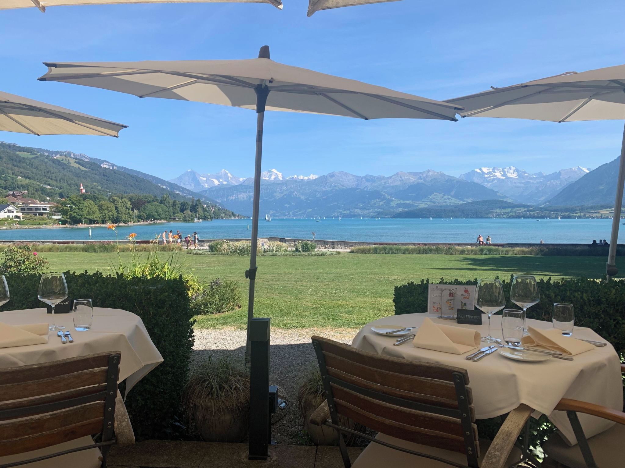 Un espace extérieur aménagé pour les repas, avec des tables et des parasols, offrant une vue sur un lac et des montagnes.