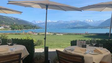 Un espace extérieur aménagé pour les repas, avec des tables et des parasols, offrant une vue sur un lac et des montagnes.