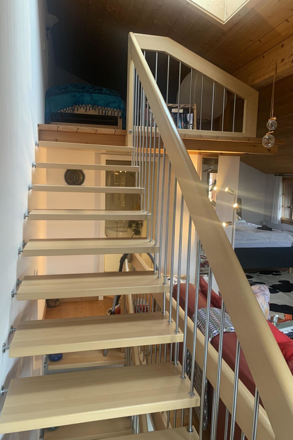 A multi-level room with a wooden staircase, a bunk bed, and a hanging light fixture.