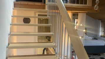 Une pièce à plusieurs niveaux avec un escalier en bois, un lit superposé et un luminaire suspendu.