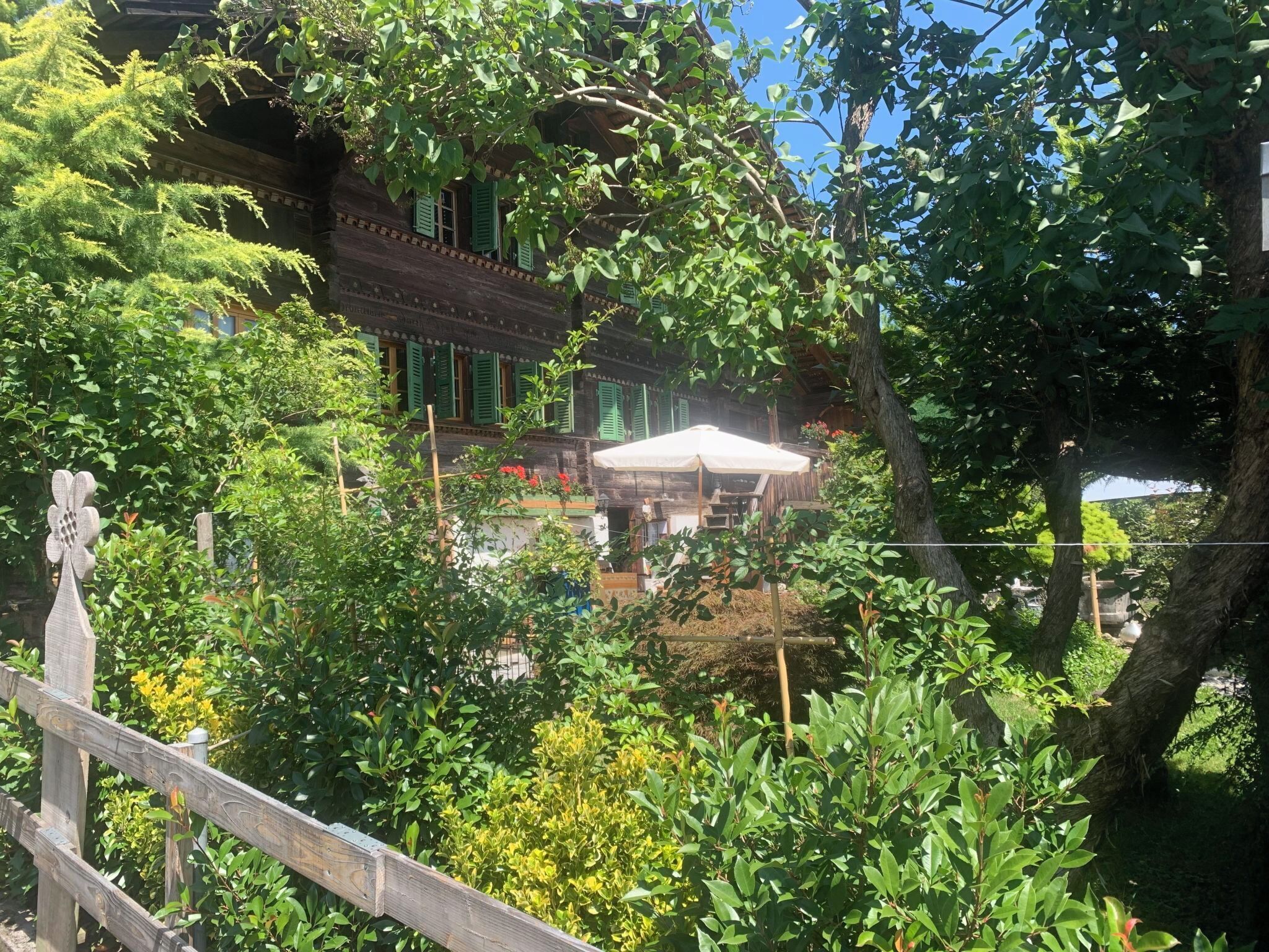 Un bâtiment traditionnel en bois, doté d’un balcon, entouré d’une végétation luxuriante et d’une clôture en bois.