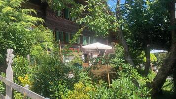Un bâtiment traditionnel en bois, doté d’un balcon, entouré d’une végétation luxuriante et d’une clôture en bois.