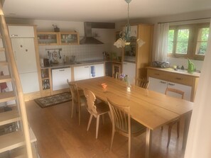 A kitchen with a wooden table and chairs, a built-in oven, and a window with curtains. - Gartenstudio "Belle Vue" Appartement/Fewo, Bad, WC, 1 Schlafraum by Interhome (Frutigen)