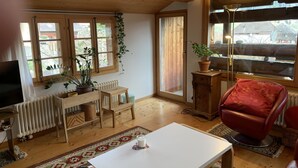 A cozy living room with wooden floors, a white table, a red chair, a TV, and a large window with a view. - Gartenstudio "Belle Vue" Appartement/Fewo, Bad, WC, 1 Schlafraum by Interhome (Frutigen)