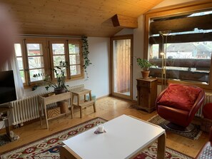 A cozy living room with wooden floors, a white table, a red chair, a TV, and a large window with a view. - Gartenstudio "Belle Vue" Appartement/Fewo, Bad, WC, 1 Schlafraum by Interhome (Frutigen)