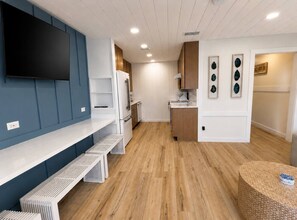 Et moderne køkken med indbyggede apparater, et fladskærms-TV og et spiseområde med et vævet bord.