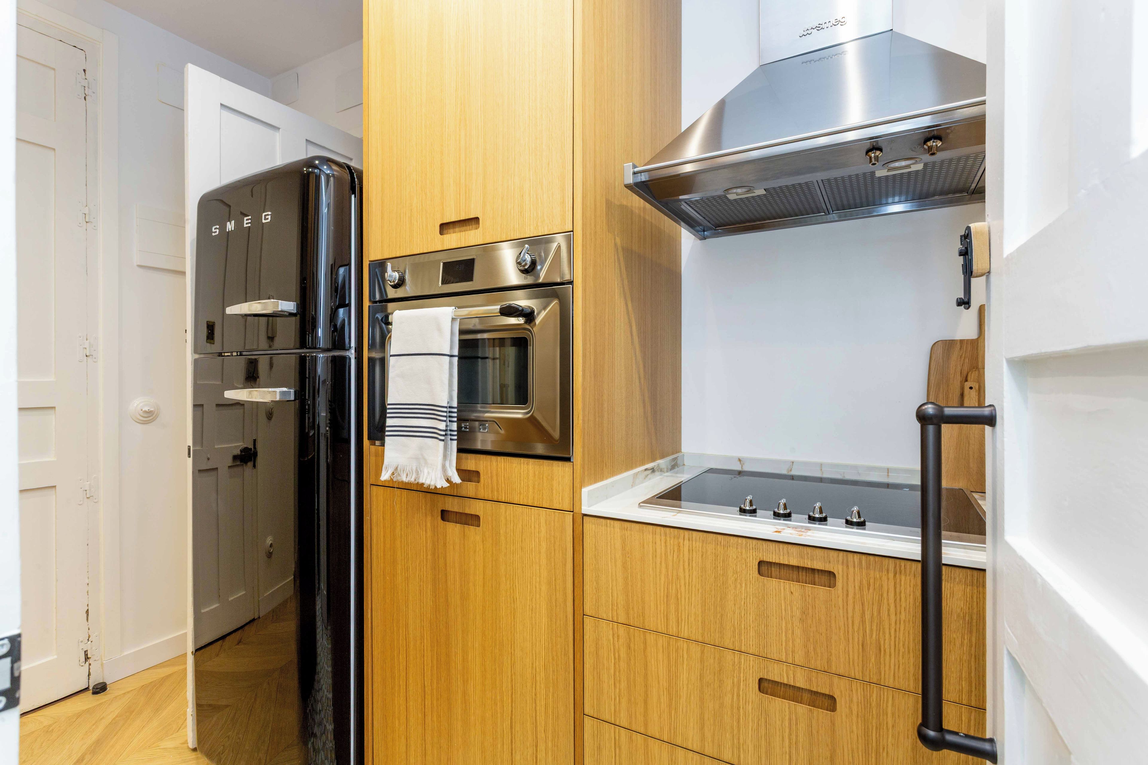 A modern kitchen with wooden cabinetry, a stainless steel refrigerator, an oven, and a built-in stove.